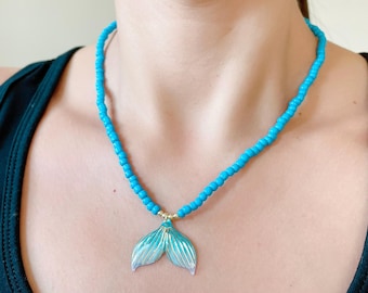 May include: A turquoise beaded necklace with a mermaid tail pendant. The pendant is made of iridescent blue and white enamel.