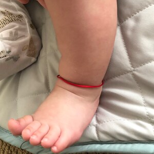 May include: A close-up of a baby's foot with a red string bracelet around the ankle.