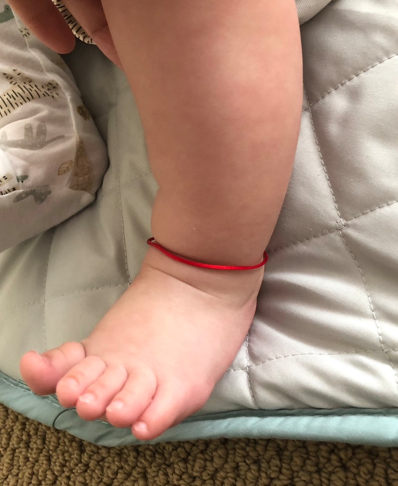 May include: A close-up of a baby's foot with a red string bracelet around the ankle.