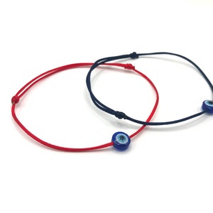 Op de afbeelding: Twee beschermende armbanden, een rode en een blauwe, met blauwe en witte boze oog bedels.