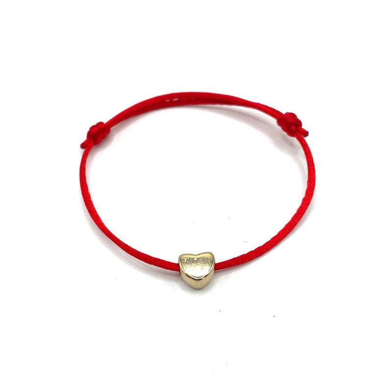 May include: A red string bracelet with a gold heart charm.