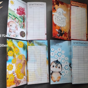 May include: Four rectangular paper savings trackers with colourful illustrations and grids labelled SPARTRACKER with columns for Datum, +/-, and Summe. Designs include a bunny, a pumpkin, sunflowers, and a penguin. Text reads Passend f&uuml;r A6 Zipperh&uuml;llen.
