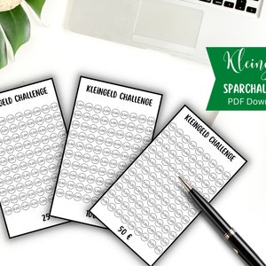 Könnte beinhalten: Drei weiße Karten mit dem Text "KLEINGELD CHALLENGE" in Schwarz gedruckt. Jede Karte hat ein Raster aus Kreisen mit Zahlen darin, die eine Spar-Challenge darstellen. Die Karten sind mit Beträgen von 25, 50€ und 100 beschriftet. Ein Stift liegt auf einer Karte.