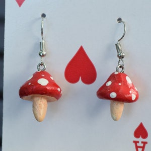 Puede incluir: Un par de pendientes de aro de champiñón rojo y blanco con ganchos plateados. Los champiñones tienen lunares blancos en los sombreros rojos.