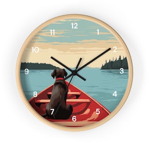 May include: A round wooden wall clock with a red canoe and a black dog sitting in the front. The clock face has white numbers and black hands. The background is a vintage-style illustration of a lake with a forest in the distance.