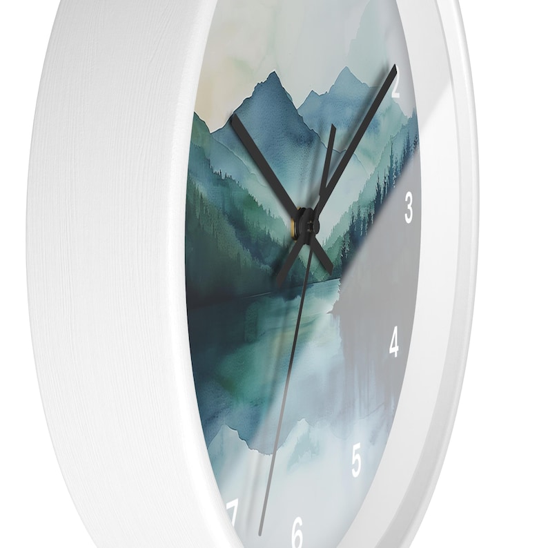 May include: A white wall clock with a watercolor landscape design. The clock face features a mountain and lake scene in shades of blue and green. Black clock hands point to the time. The clock has a white frame.