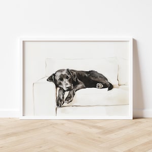 Może przedstawiać: Oprawiona akwarela przedstawiająca czarnego psa odpoczywającego na białej sofie. Pies leży, a jego głowa i przednie łapy zwisają z krawędzi sofy. Grafika jest w białej ramie.
