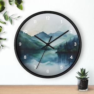 May include: Round wall clock with a black frame. The clock face features a watercolor landscape of mountains, trees, and a lake in shades of blue and green. The clock hands are black, and the numbers are white.
