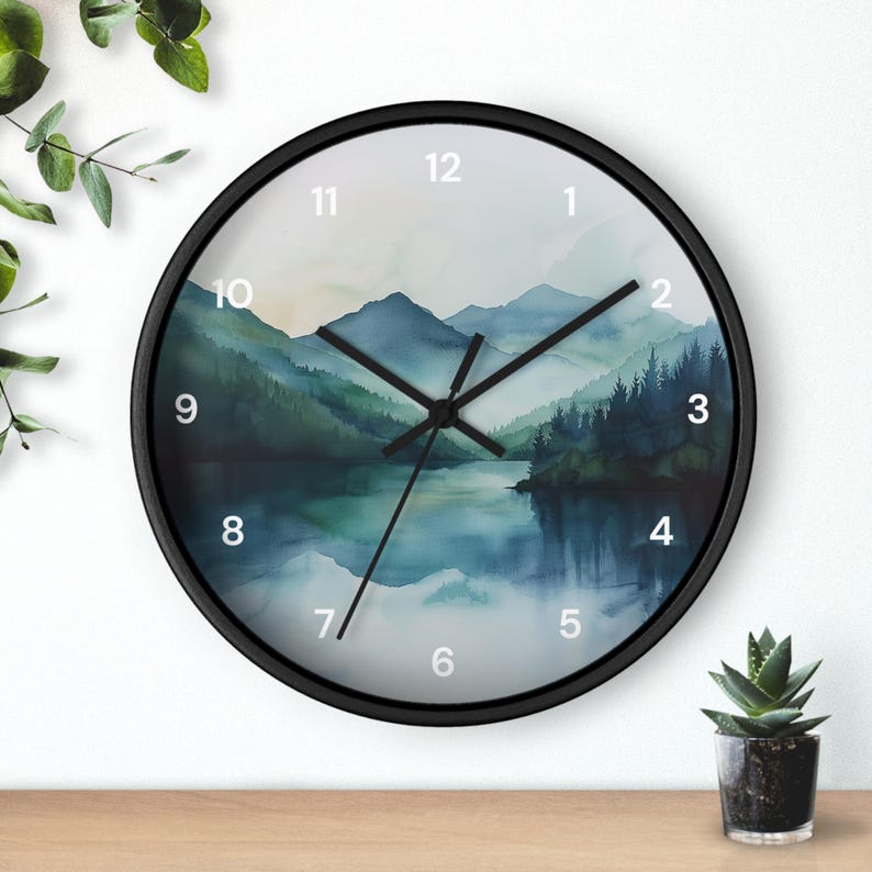 May include: Round wall clock with a black frame. The clock face features a watercolor landscape of mountains, trees, and a lake in shades of blue and green. The clock hands are black, and the numbers are white.