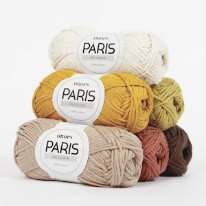 Könnte beinhalten: Ein Stapel bunter Wollknäuel in Creme, Senfgelb, Olivgrün und Braun. Jedes Knäuel trägt ein Etikett mit der Aufschrift "DROPS PARIS UNI COLOUR 100% Cotton". Ideal zum Stricken und Häkeln.