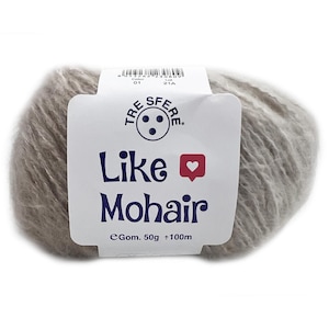 Könnte beinhalten: Ein Knäuel hellgrauer Mohairwolle mit einem weißen Etikett. Das Etikett trägt den Text "Like Mohair" in Marineblau, ein rotes Herz und den Markennamen "TRESFERE". Das Garn ist 50g + 100m.