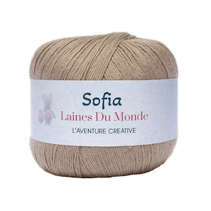 Op de afbeelding: Een bol beige garen met een wit etiket. Het etiket leest "Sofia Laines Du Monde" met een kleine teddybeer-afbeelding. De tekst "L'AVENTURE CREATIVE" staat er ook op. Perfect voor brei- en haakprojecten.