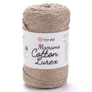 Può includere: Una matassa di filato YarnArt Macrame Cotton Lurex beige con fili metallici dorati. L'etichetta mostra il nome del marchio e i dettagli del prodotto. Il filato è adatto per progetti di macramè. Peso 250g.