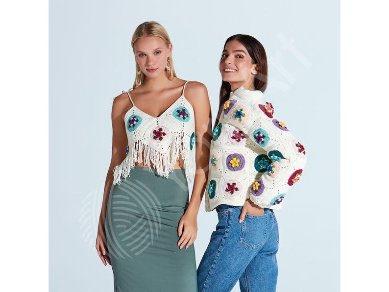 May include: Two women modeling crochet tops and a jacket. The white crochet top has a fringe hem and colorful floral designs. The jacket is also white with similar floral patterns. One woman wears a green skirt, the other blue jeans.