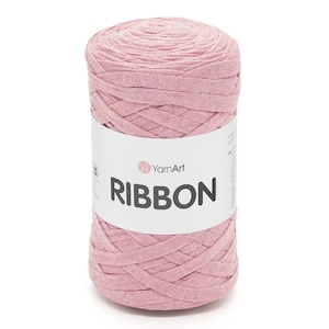 Könnte beinhalten: Eine zylindrische Spule aus rosa Bandgarn. Das Garn ist eng gewickelt, mit sichtbarer Textur und einer weichen, gedämpften Farbe. Ein weißes Etikett umschließt die Spule und zeigt den Markennamen "YarnArt" und das Wort "RIBBON" in fetten, schwarzen Buchstaben.