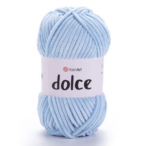 Può includere: Un gomitolo di filato azzurro con la parola "dolce" stampata sull'etichetta. Il filato è spesso e morbido, ideale per progetti di maglieria o uncinetto. L'etichetta include anche il marchio "YarnArt".