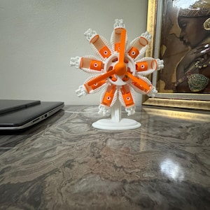 Può includere: Un modello di motore radiale bianco e arancione con un'elica centrale e nove cilindri disposti in uno schema circolare. L'assemblaggio meccanico è montato su una base e un supporto circolari bianchi, mostrando un design dettagliato stampato in 3D.