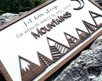Op de afbeelding: Een houten bord met de tekst "Let him sleep... for when he wakes he will move MOUNTAINS" en een halve maan. Het bord heeft vijf houten bergen met ingewikkelde ontwerpen.