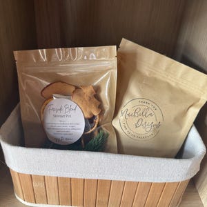 May include: Two brown paper pouches in a bamboo basket. The left pouch is clear-fronted, containing dried fruit and pine, labeled 'Fireside Blend Simmer Pot'. The right pouch is opaque brown paper with the text 'Thank You MacBella Designs'.