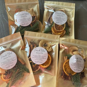 May include: Five clear, resealable pouches containing a Fireside Blend simmer pot mix. Each pouch holds dried orange slices, cinnamon sticks, star anise, and evergreen sprigs, with a round white label featuring black text and a script logo.