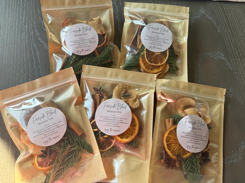 May include: Five clear, resealable pouches containing a Fireside Blend simmer pot mix. Each pouch holds dried orange slices, cinnamon sticks, star anise, and evergreen sprigs, with a round white label featuring black text and a script logo.