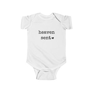 May include: White baby onesie with black text that reads "heaven sent" with a small heart symbol.