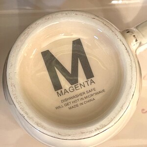 May include: White ceramic mug with a black letter "M" and the word "MAGENTA" printed on the side. The mug also has the text "Dishwasher Safe, Will Get Hot in Microwave, Made in China".