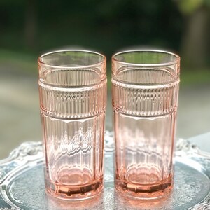 May include: Two pink glass tumblers with a ribbed design. The glasses are sitting on a silver tray.