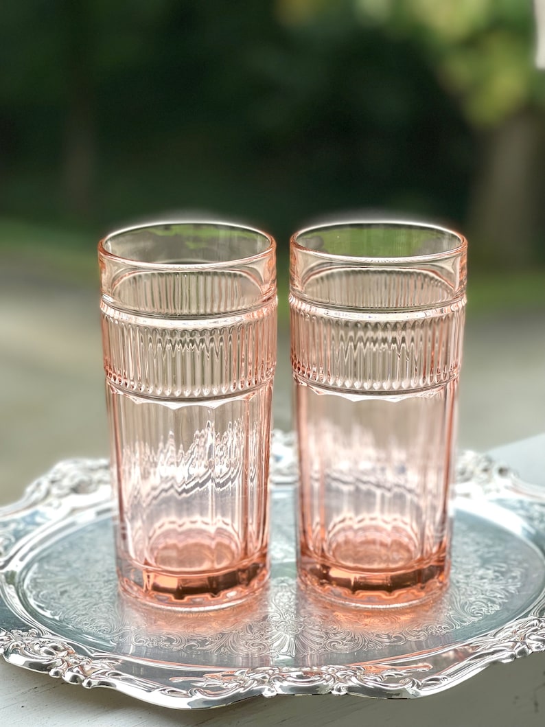 May include: Two pink glass tumblers with a ribbed design. The glasses are sitting on a silver tray.