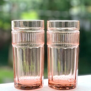 May include: Two clear pink glass tumblers with a ribbed design. The glasses are empty and sitting on a white surface.