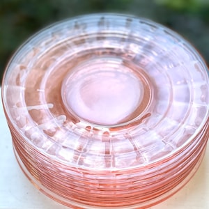 May include: A stack of pink glass dessert plates with a fluted design.