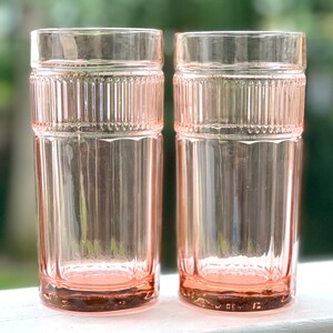 May include: Two pink glass tumblers with a ribbed design. The glasses are clear and have a pink tint.