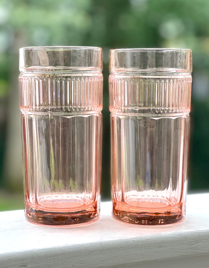 May include: Two pink glass tumblers with a ribbed design. The glasses are clear and have a pink tint.