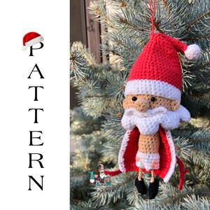 May include: A crocheted Santa Claus ornament with a red hat, white beard, and a red and white cape. The ornament is hanging from a tree branch.
