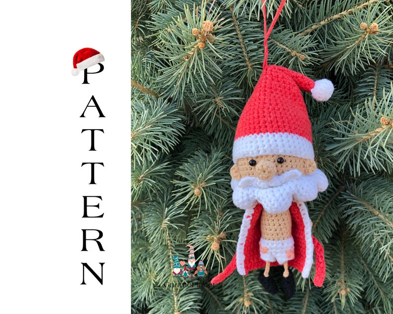 May include: A crocheted Santa Claus ornament hanging on a green Christmas tree. The ornament is red and white with a white beard and black eyes. The ornament has a red hat with a white pom-pom.