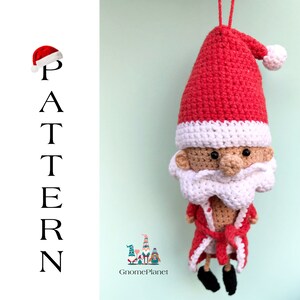May include: Crocheted Santa Claus ornament with a red hat, white beard, and a red robe. The ornament is hanging from a string and has a white pom-pom on the top of the hat. The ornament is against a light green background.
