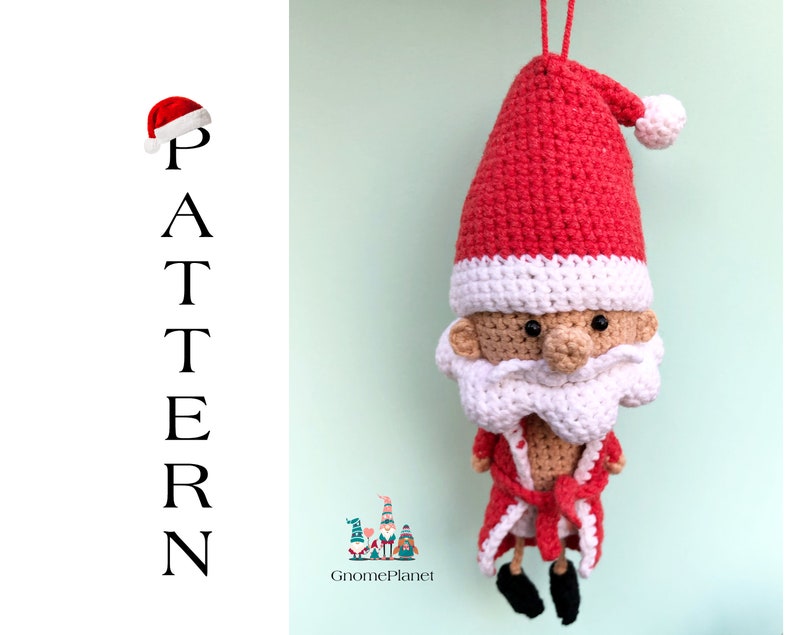 May include: Crocheted Santa Claus ornament with a red hat, white beard, and a red robe. The ornament is hanging from a string and has a white pom-pom on the top of the hat. The ornament is against a light green background.