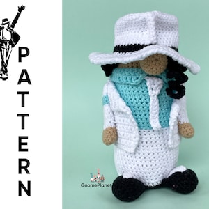 Puede incluir: Muñeca de crochet de una estrella del pop que lleva un traje blanco, un fedora negro y una camisa azul claro. La muñeca está de pie sobre un fondo verde.
