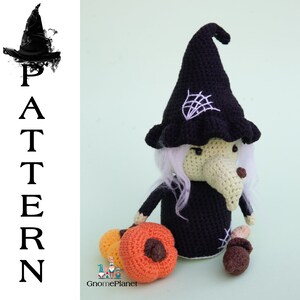 May include: Crocheted witch doll with a black hat, white hair, and a long nose. The doll is holding a small orange pumpkin and a brown acorn. The doll is sitting on a green background.