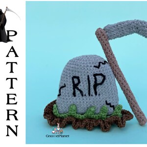 May include: A crocheted gray tombstone with the words "RIP" on it, a brown crocheted scythe, and green crocheted grass.