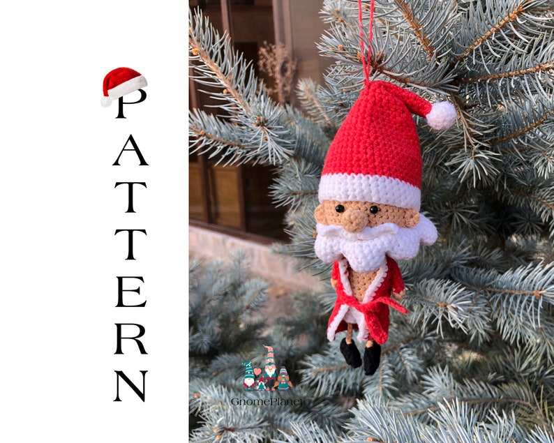 May include: Crocheted Santa Claus ornament hanging from a pine tree branch. The ornament is red and white with a white beard and a red hat. The ornament is a handmade craft.