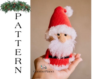 Pode incluir: Boneca de Papai Noel de crochê com um chapéu vermelho, barba branca e cinto preto. A boneca está sendo segurada na mão de uma pessoa.