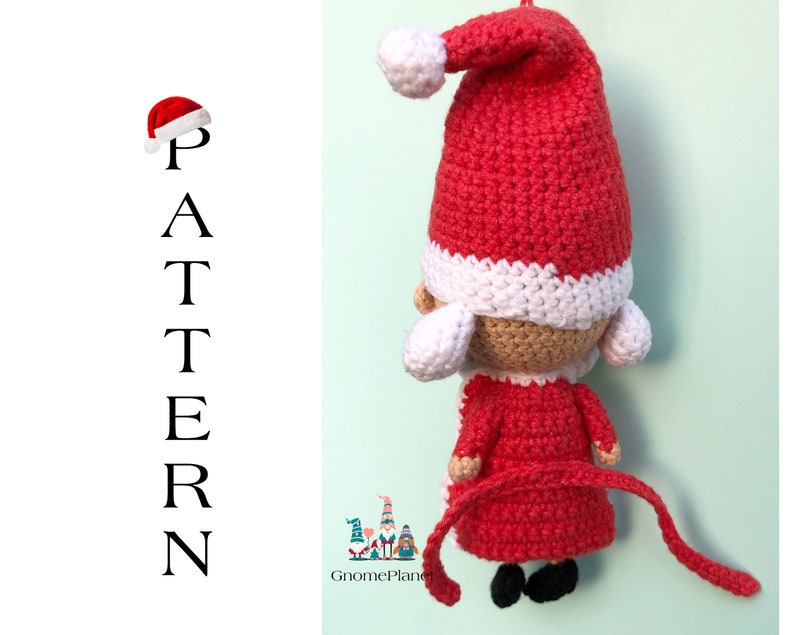 May include: Crocheted Santa Claus ornament with a red hat, white trim, and a long red tail. The ornament is made with red, white, and beige yarn.