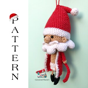 May include: Crocheted Santa Claus ornament with a red hat, white beard, and red and white coat. The ornament is hanging from a string and has a white background.