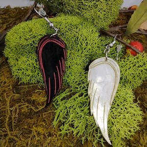 May include: A pair of dangle earrings featuring a black and red wing on one side and a white wing on the other side. The wings are made of a shiny material and have a delicate design.