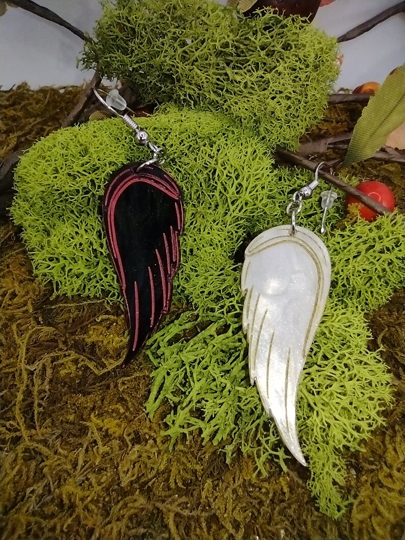 May include: A pair of dangle earrings featuring a black and red wing on one side and a white wing on the other side. The wings are made of a shiny material and have a delicate design.