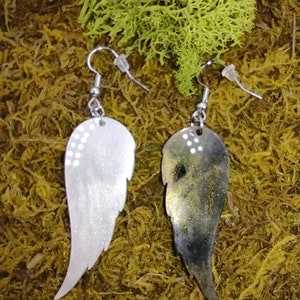May include: A pair of silver earrings with a wing design. One wing is silver with white glitter and the other wing is black with gold glitter.