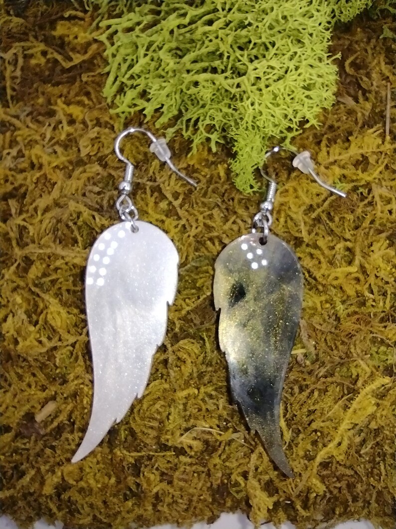 May include: A pair of silver earrings with a wing design. One wing is silver with white glitter and the other wing is black with gold glitter.