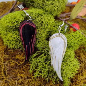 May include: A pair of dangle earrings featuring a black and red wing on one side and a white wing on the other. The wings are crafted from wood and have a painted finish.