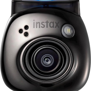 Peut inclure: Un appareil photo instantané Instax noir avec une face argentée et un objectif proéminent. L'appareil photo a une forme arrondie, un flash et le logo Instax. Une lumière bleue est visible en haut.